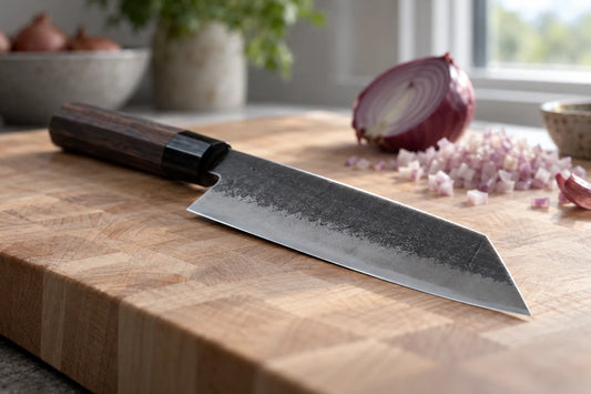 Bunka knife with a tall blade and angled reverse-tanto tip on a maple cutting board beside a halved red onion
